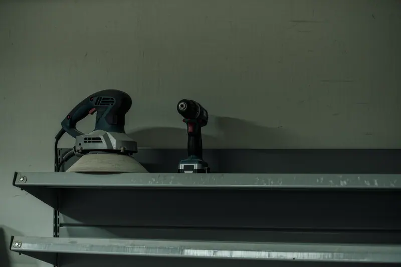 Hire power tools and a stripped floor sander standing on a steel shelf in a plain store room.